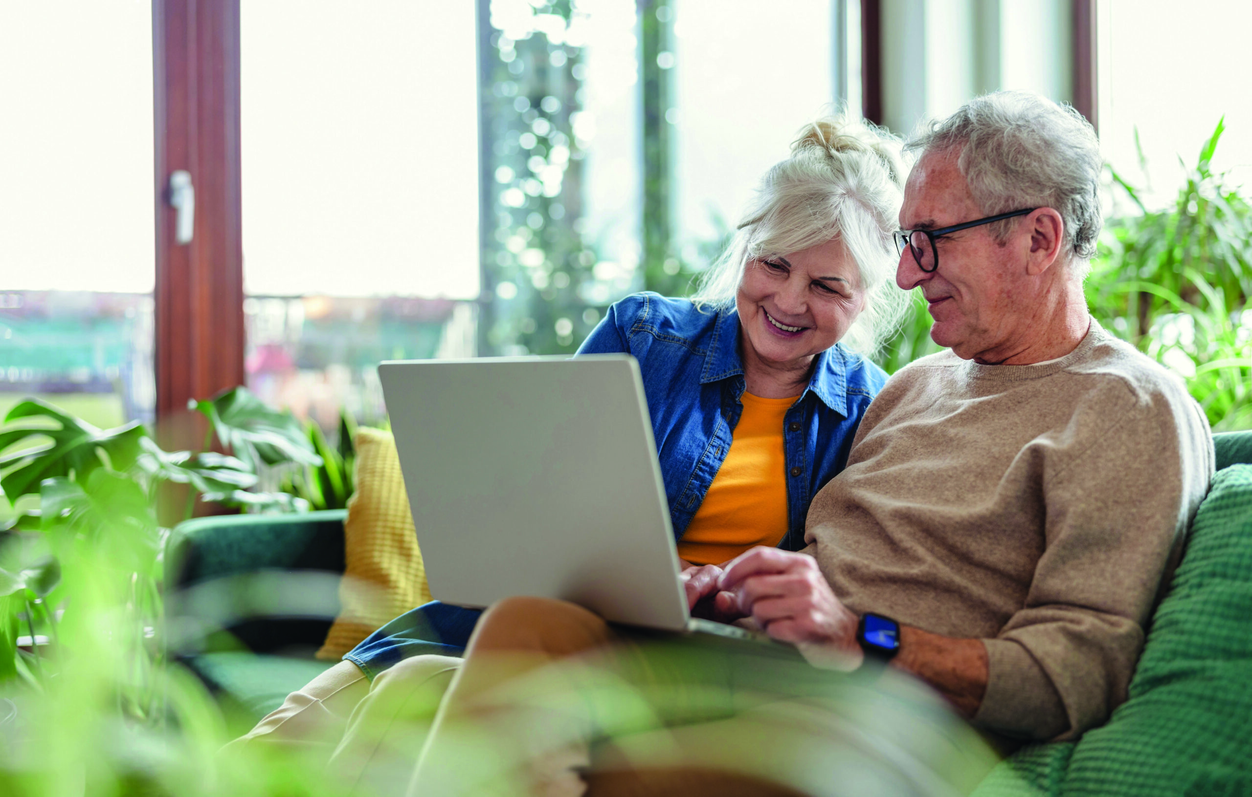 Senior,Couple,Using,Laptop,While,Sitting,On,Sofa,In,Living